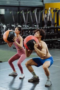 A man and woman exercising with medicine balls in a gym setting, focusing on strength and fitness.