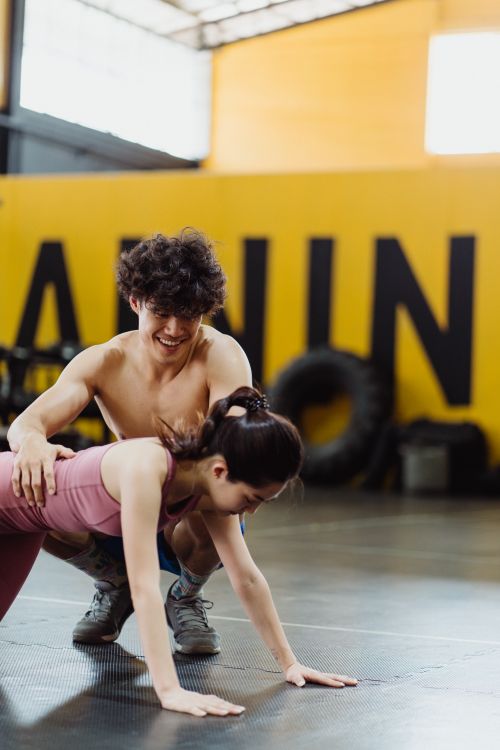 Free A man assists a woman during a push-up exercise in an indoor gym setting, emphasizing teamwork. Stock Photo