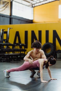 A personal trainer helps a woman with her plank exercise in a gym setting.