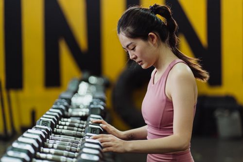 Free A woman in activewear choosing weights at a modern gym. Indoor fitness setting. Stock Photo