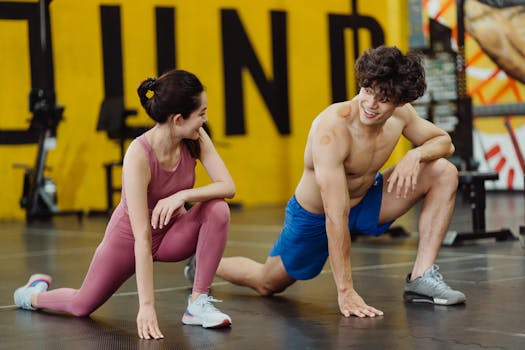 A diverse couple in sports clothing, smiling and stretching together at an indoor gym.