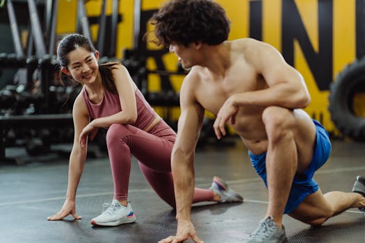Two young adults stretching on the gym floor, focused on fitness and flexibility.