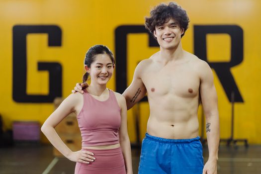 一对穿着运动服的情侣面带微笑，自信地站在充满活力的健身房中