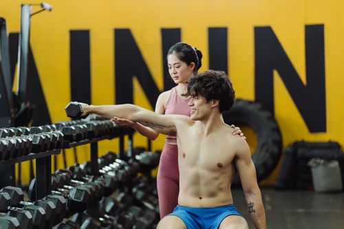 Free Young man lifting weights with a woman trainer assisting in a gym setting. Stock Photo