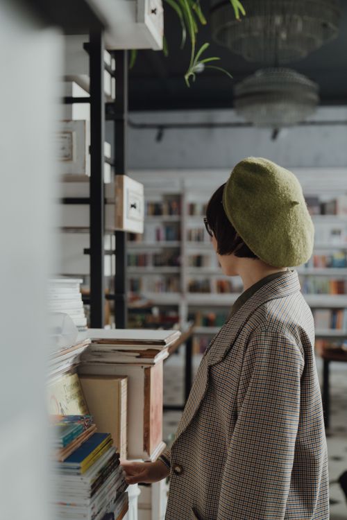 Free A woman in a beret and checked coat explores a cozy bookstore filled with bookshelves and literature. Stock Photo