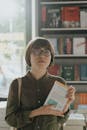 一名年轻女子站在书店里，手里拿着一本书，周围摆满了文学书架