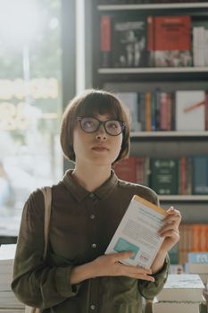 一名年轻女子站在书店里，手里拿着一本书，周围摆满了文学书架