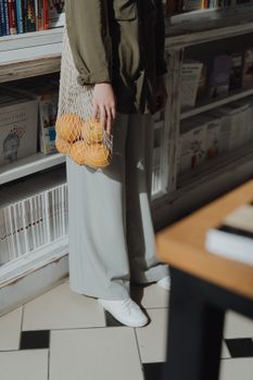 一名妇女在书店里拿着装有橙子的环保袋，体现了休闲且可持续的购物理念