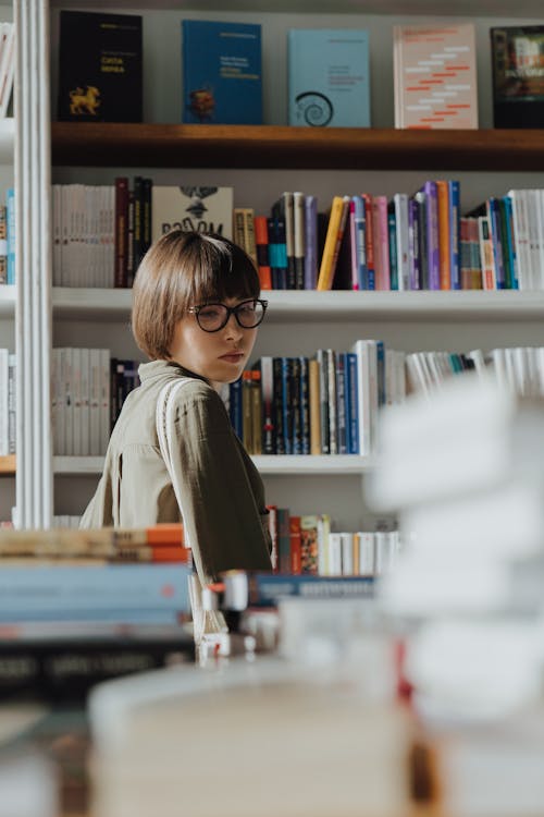 Woman in Gray Long Sleeve Shirt Standing in Front of Books