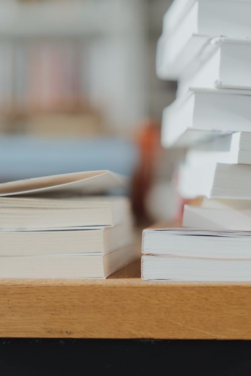 Free Close-up of stacked white books on a wooden table in a quiet library setting. Stock Photo