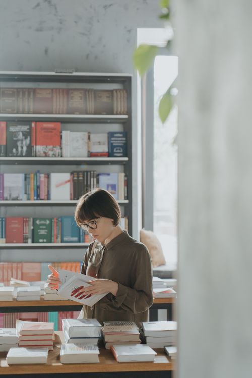 Free A woman reads attentively in a tranquil bookstore setting with bookshelves in the background. Stock Photo