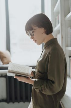 在舒适的图书馆里，一名戴眼镜的年轻女子正在看书