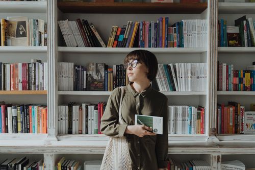 Free A woman holds a book in a cozy bookstore, enjoying the peaceful atmosphere and wide selection of literature. Stock Photo