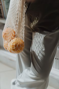 特写镜头：一名妇女在室内用可重复使用的线袋装着有机橙子