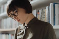 在现代图书馆里，一位戴着眼镜的年轻女子正专注地阅读，显得深思熟虑