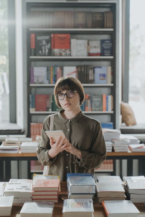Free A young woman with glasses exploring books in a cozy bookstore setting. Stock Photo