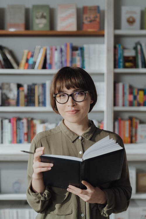 Wanita Dengan Kemeja Kancing Hijau Mengenakan Buku Bacaan Kacamata Berbingkai Hitam