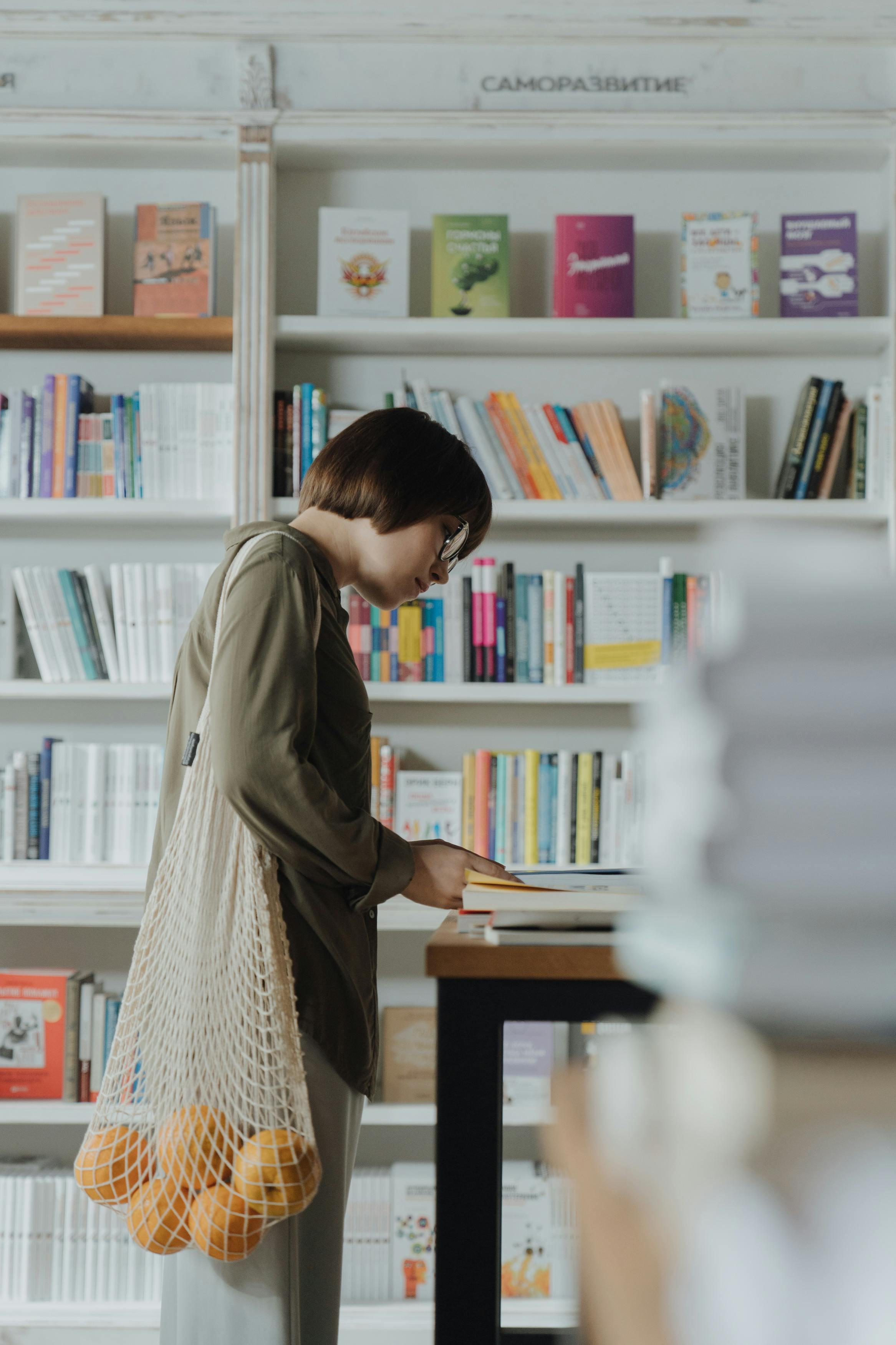 woman in gray long sleeve dress standing in front of book shelf