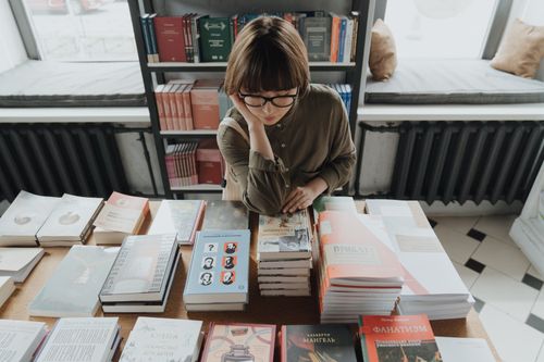Free A young woman with glasses browsing books in a cozy bookstore. Stock Photo