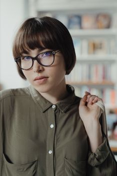 一位戴着眼镜的年轻女子站在图书馆里，肖像传达出智慧与休闲的气息