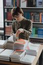 一位女士在一家舒适温馨的书店里浏览书籍，四周堆满了文学作品