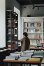 一位女士正在一家舒适明亮、光线充足的书店里，浏览着不拘一格的书籍