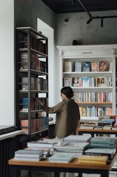 一位女士正在一家舒适明亮、光线充足的书店里，浏览着不拘一格的书籍