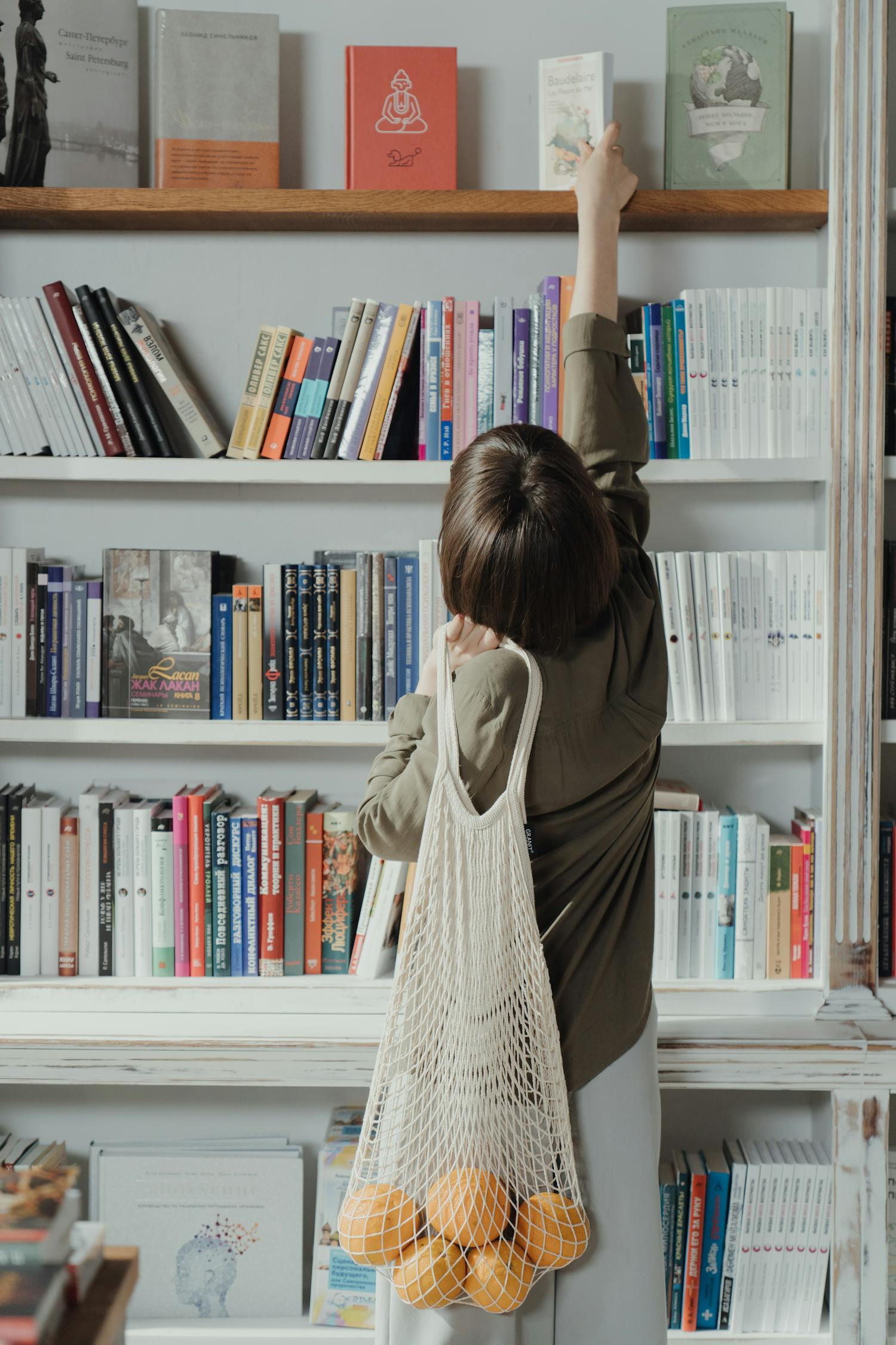 Woman in Beige Long Sleeve Dress Standing in Front of White Wooden Book Shelf