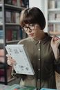 一位戴眼镜的年轻女子在图书馆里读书，这有助于学习和获取知识
