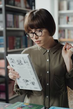 一位戴眼镜的年轻女子在图书馆里读书，这有助于学习和获取知识