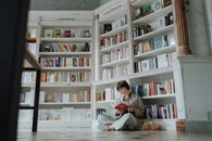 一名妇女坐在一家现代书店里看书，店内优雅的白色书架上摆满了色彩缤纷的书籍