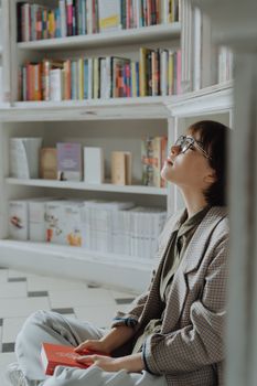 在宁静的图书馆里，一名年轻女子坐在书架旁，沉浸在一本书中