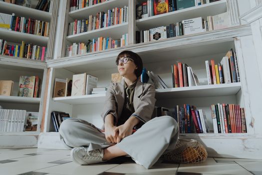 一名女子舒适地坐在图书馆的书架间，四周弥漫着放松与求知的氛围