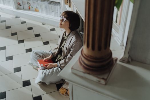 在宁静的图书馆里，一位女士若有所思地坐在地板上，手里拿着一本红书
