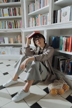 一位年轻女子在现代图书馆里坐在地板上，轻松地享受阅读一本书的时光