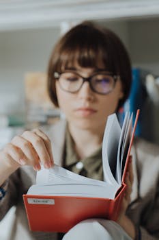 A focused young woman flipping through a book in a cozy indoor library setting.
