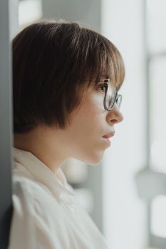 一位戴着眼镜的年轻女子凝视着窗外，若有所思，透露出智慧与好奇
