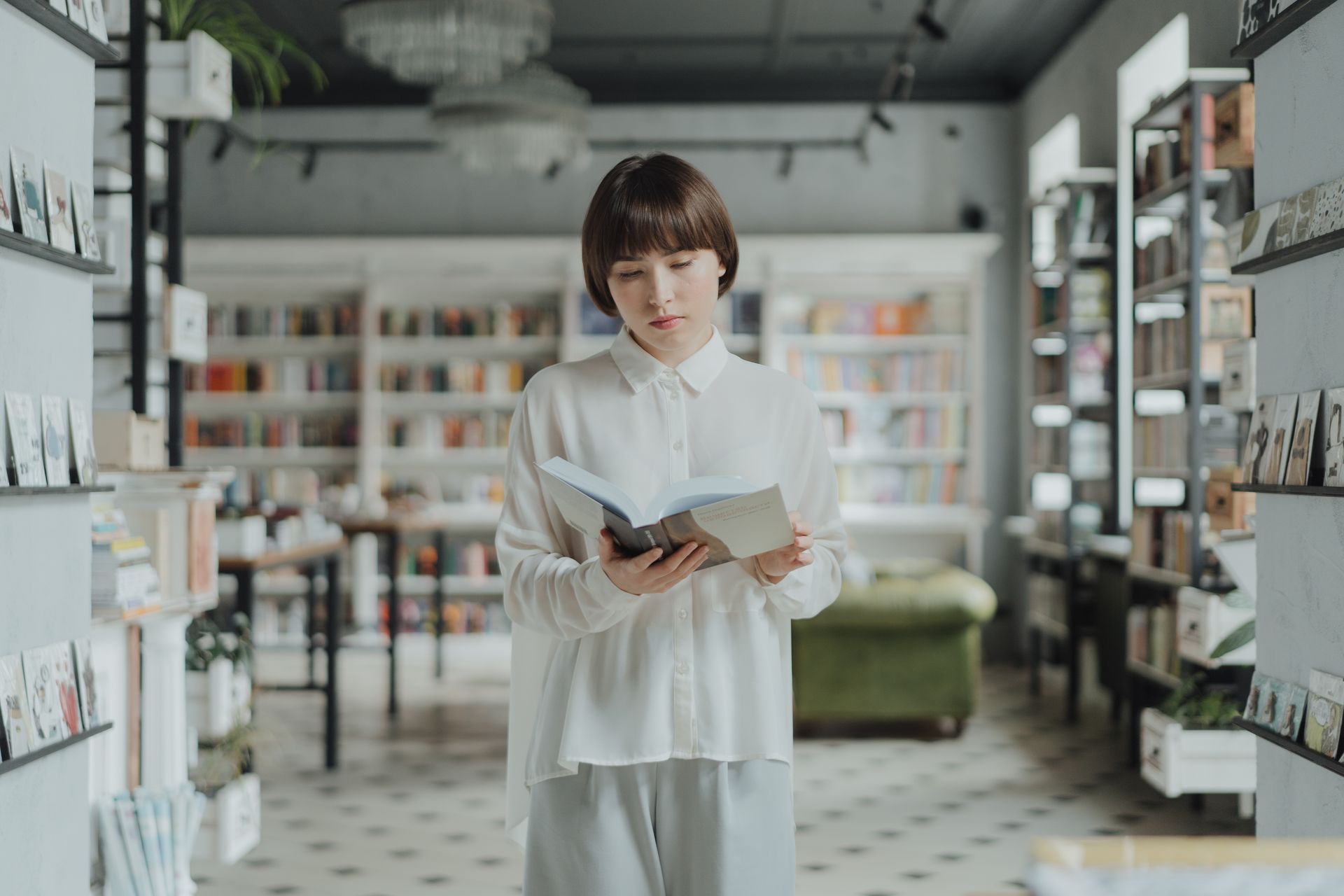 A young woman in a modern bookstore reading a book, surrounded by shelves of literature.