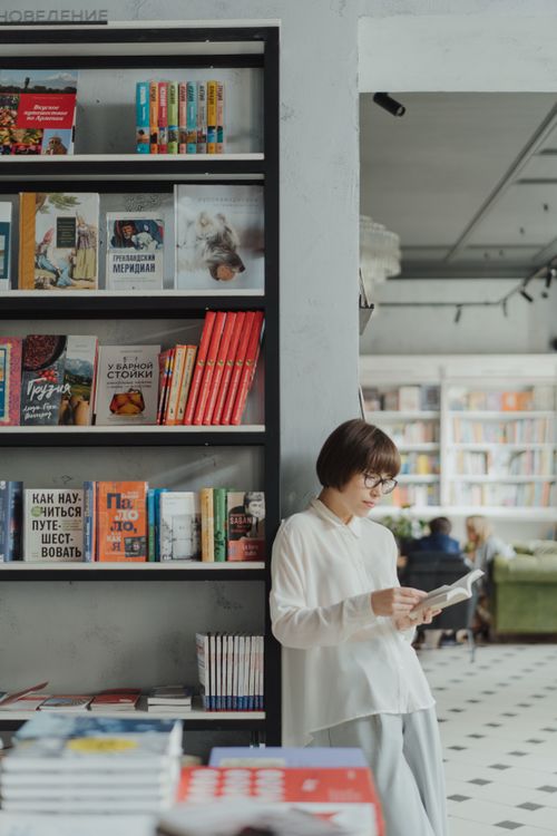 Free Young woman reading by a bookshelf in a contemporary bookstore setting. Stock Photo