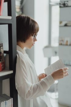 一位穿着白衬衫的女人在现代图书馆的书架旁看书