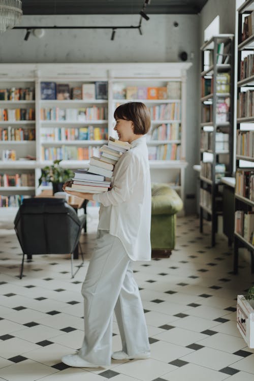 Woman in White Long Sleeve Shirt Carrying a Stack of Books