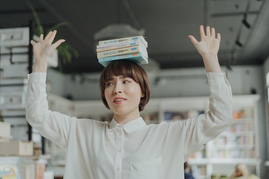 A woman skillfully balances a stack of books on her head in a lively library setting.