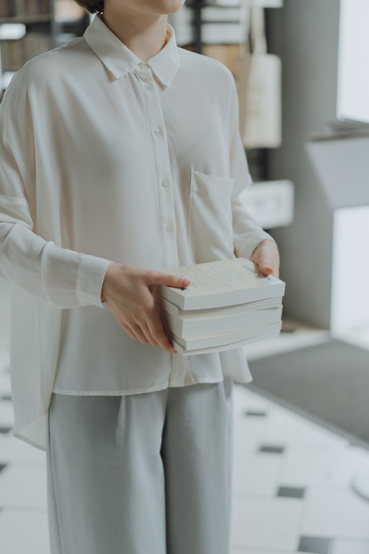 Person In White Long Sleeve Shirt Carrying A Stack Of Books