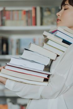 一名女子穿着白色长袖，拿着一大堆书，在图书馆里显得不知所措