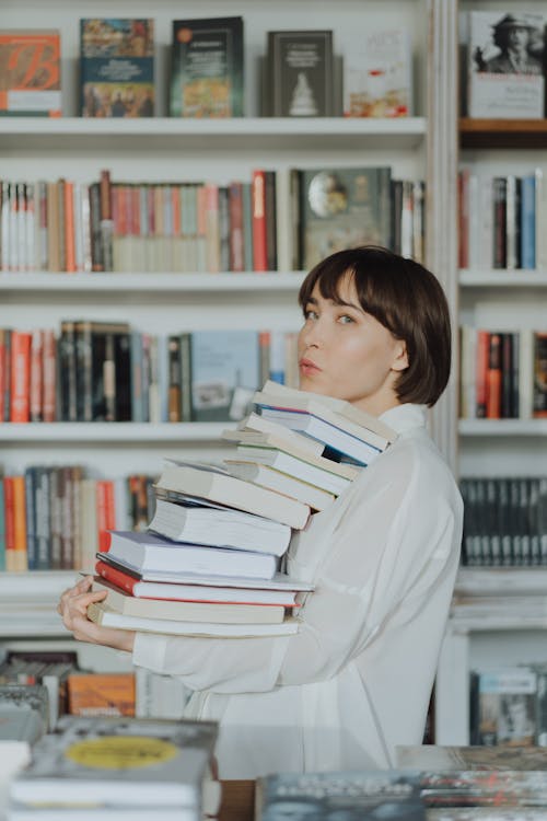 Free Woman in White Long Sleeve Shirt Carrying a Stack of Books Stock Photo