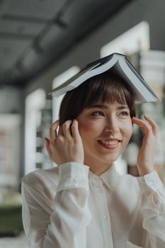 一位微笑的女人在图书馆里，把一本打开的书顶在头上，享受着休闲阅读
