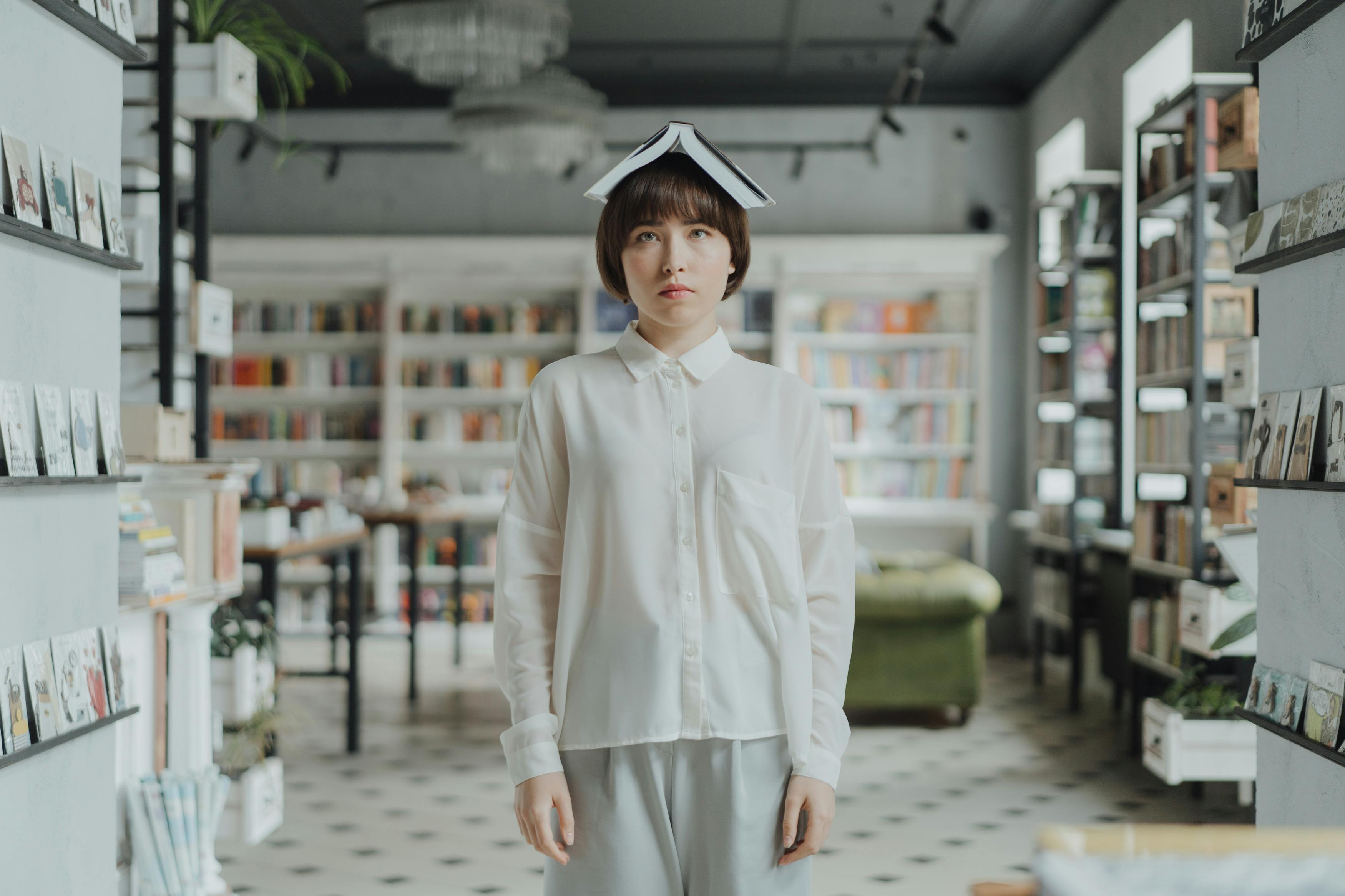 Young woman in white shirt balancing a book on her head in a modern library setting.