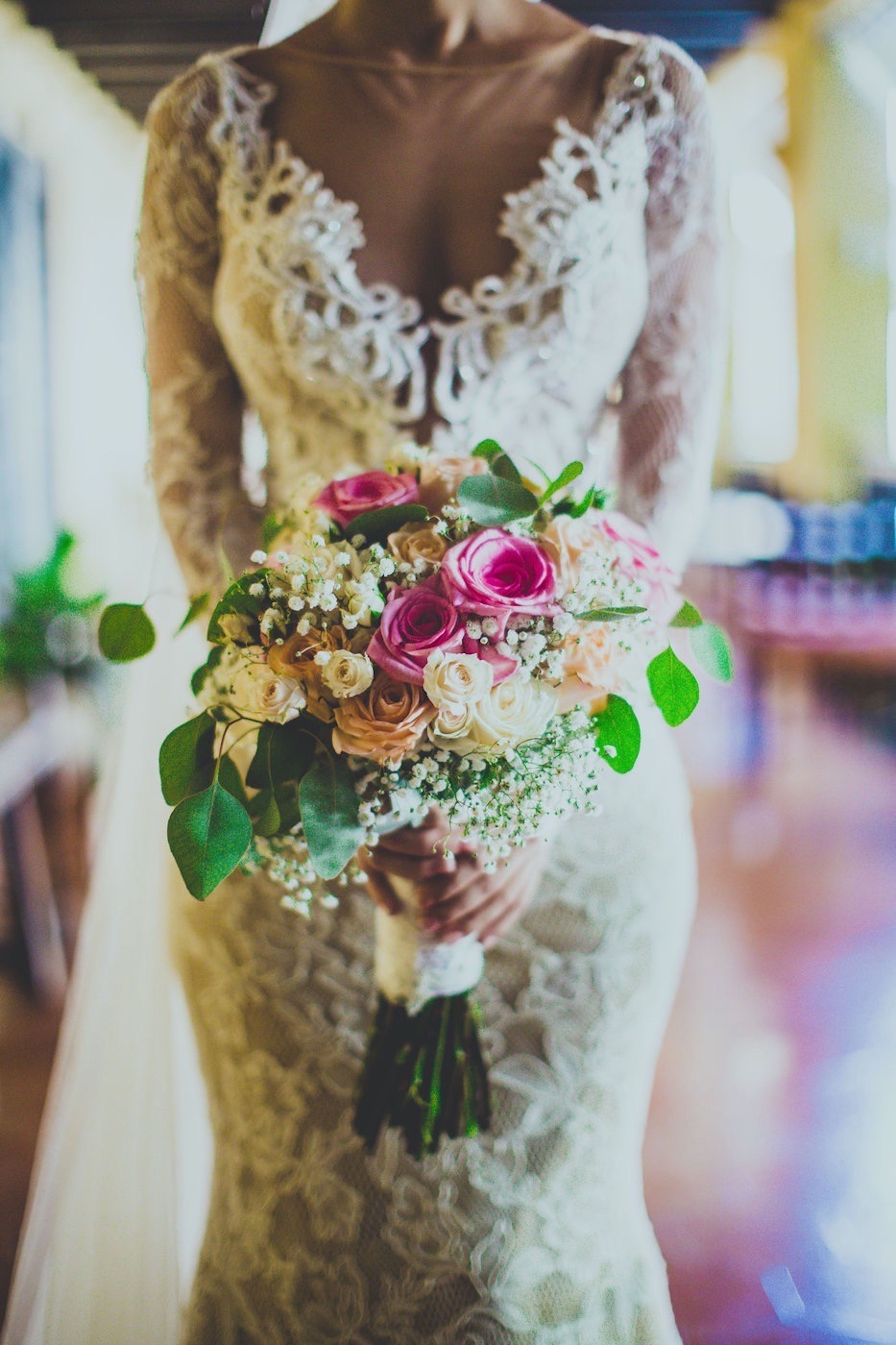 Crop anonymous bride in posh white dress with low neckline holding fragrant delicate bouquet in wedding hall