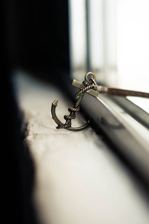 Free Soft focus of metal stylish charm in anchor shape with leather strap placed on grunge windowsill Stock Photo