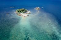 Drone view of turquoise shallow sea with small cay covered with lush tropical greenery in sunlight